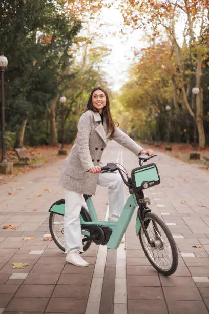 Portrait of smiling young latin woman riding an electric-bike in a park. High quality photo