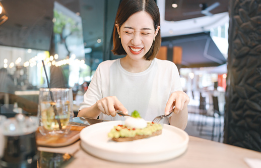 Weekend city break people lifestyle concept. Young adult asian foodie woman eating healthy food diet meal. At indoors cafe restaurant on day. Happy smile face and short hair person.