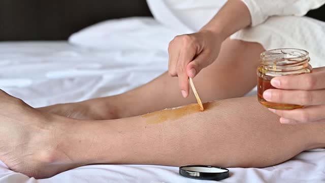 Close-up of woman applying soft wax on her leg before removal hair grows by using wax strips.