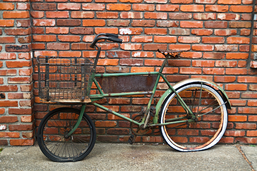 Vintage green bicycle with wire basket leaning against rustic brick wall in urban setting evokes nostalgia and eco-friendly transport. Perfect for businesses promoting sustainability, urban lifestyle, or historical themes.