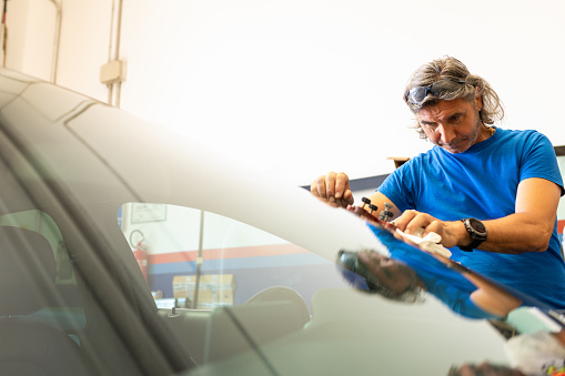 Glazier in blue shirt looks at the windshield of a car after repairing it. High quality photo