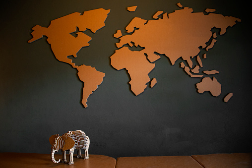 World map and elephant figurine on wooden table with blackboard background