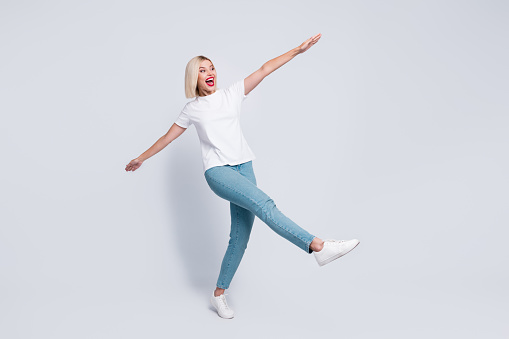 Full body photo of ecstatic crazy woman wear stylish t-shirt hold arms like wings look empty space isolated on gray color background.