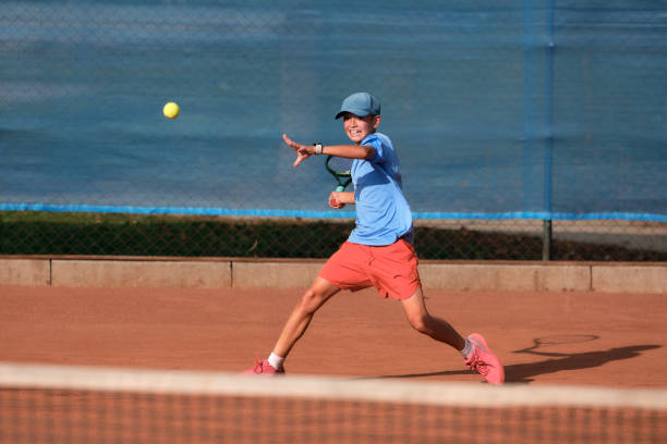 un jeune garçon caucasien joue au tennis sur un court orange en fin d’après-midi. - tennis child athlete sport photos et images de collection