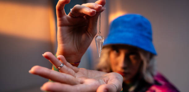 close up of blonde woman holding and examining amethyst crystal on silver chain at neon studio light - fortune telling paranormal neon light prophet imagens e fotografias de stock