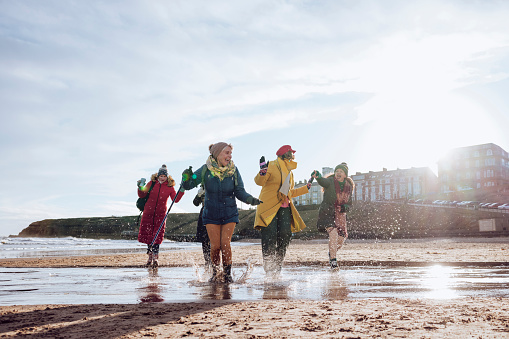 A group of mature female friends on a walk in Tynemouth, North East England. They are enjoying time outside on a beach, running and laughing together.