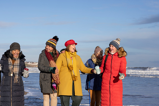 Group of mature female friends on a walk in Tynemouth, North East England. They are enjoying time outside on a beach.