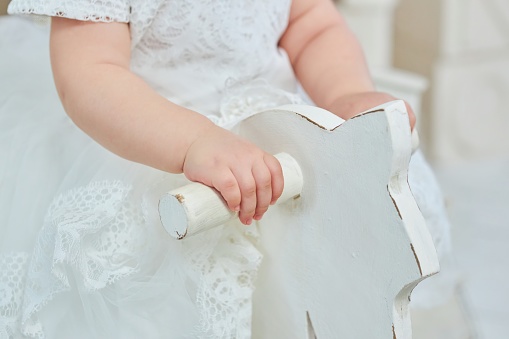 Baby girl's baby hands hold onto a wooden rocking horse. Entertainment for young children