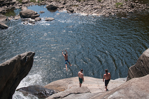 Canaan, Connecticut. July 28, 2019. A man jumping off of rocks into water at Great Falls in Falls Village Canaan Connecticut on a sunny summer day.