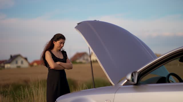 Stressed woman open hood and looking on broken car engine