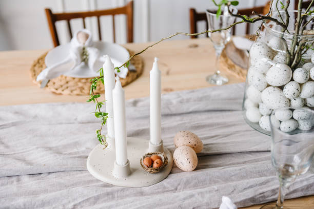 istock Easter decor with candles, easter quail eggs in nest, vase with twig, branch, leave at home. Setting table for festive dinner. Holidays celebration concept. Interior design of dining room. Closeup. 1922154677