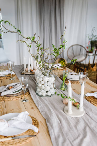 dressage de la table pour le dîner de pâques avec bougie, assiettes en céramique avec des œufs de pâques dans le nid, lapin en serviette en lin. concept de célébration des fêtes. décor avec vase avec brindille, branche, laisser à la maison. insta - retro revival food easter napkin photos et images de collection