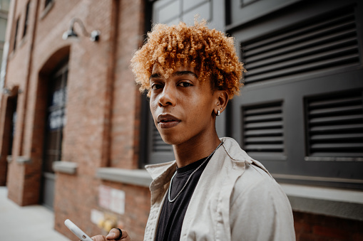 Portrait of the young african american man with serious expression leaning on the wall at street of city. Curly millennial teenager looking at the camera