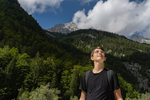A teenager walks through the forests in the mountains and enjoys the greenery, the river, and the fresh air.