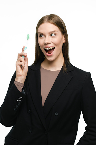 The girl smiles widely, holding a toothbrush in her hands and showing beautiful straight teeth with braces.