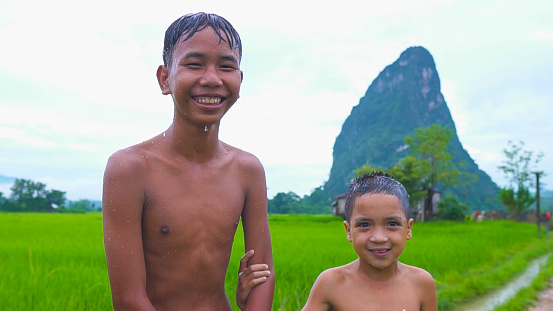 Older brother hugs younger brother ,by the neck, shoulders with big smile on green mountain background in a countryside Laos.