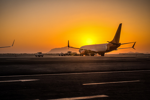 Preparation of passenger airplane before flight. Airport at the colorful sunset or sunrise. Transportation theme