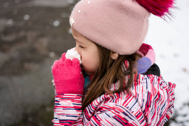 Girl blowing nose at park during snowy winter day.