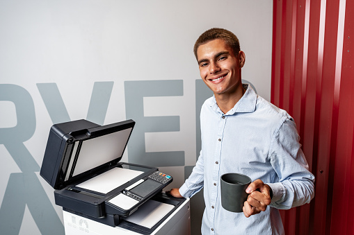 Positive young man using printer in the modern office close up