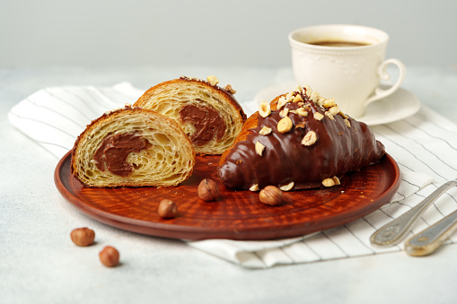 Chocolate croissant on clay plate with cup of coffee on table close up