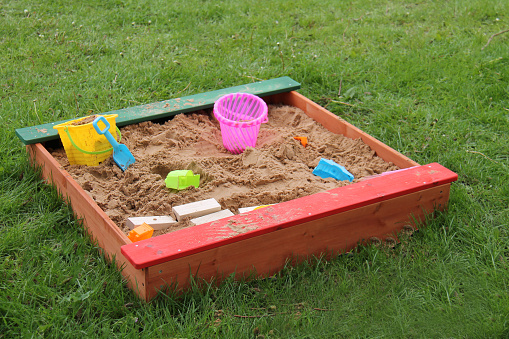 A Wooden Sandpit with Some Plastic and Wood Toys.
