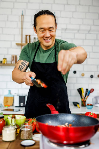 istock Smiling chef puts spices while fries vegetables 1922221859