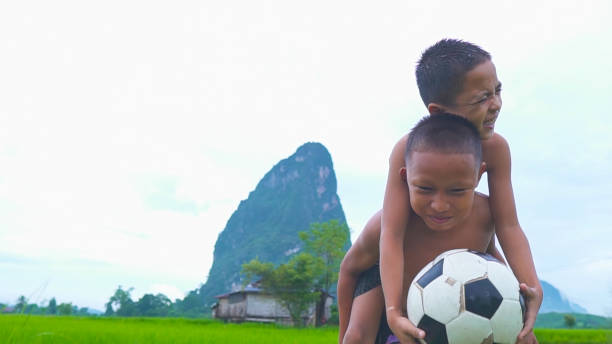two children enjoying with football in green mountain background in a countryside laos. - family with one child family two parent family father ストックフォトと画像