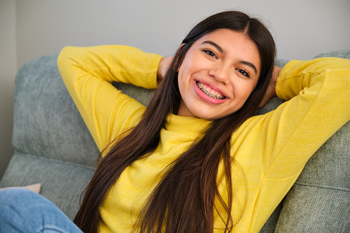Female teenager with braces smiling relaxing on a sofa at home. Wellbeing.