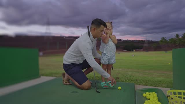 Happy little girl having fun at the driving range with her dad
