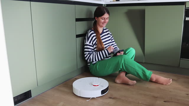 Woman Using Robot Vacuum Cleaner at Her Modern Kitchen