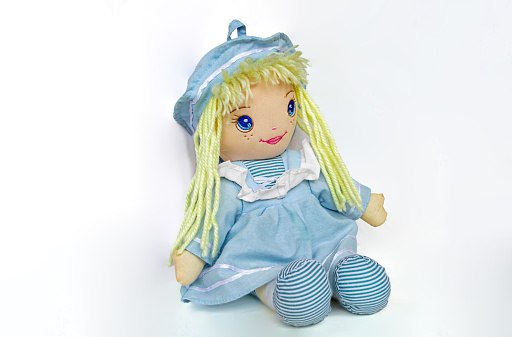 A beautiful doll with blond hair and a blue dress sits on a white background