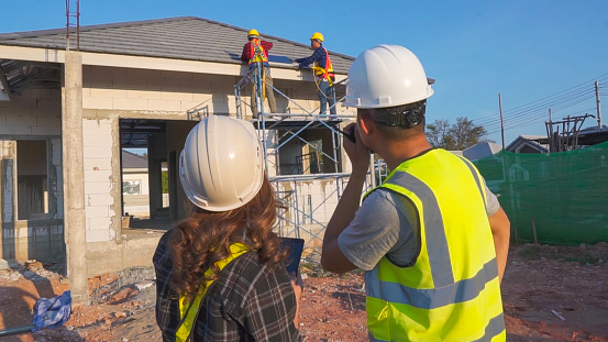 Asian male construction engineer talking to Asian female architects. standing at a construction site to explain install solar cells on the roof of the house.
