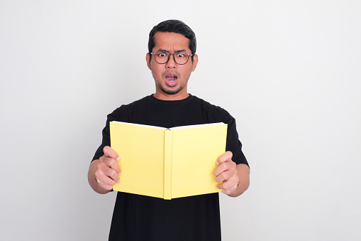 Adult Asian man showing shocked face expression when reading a book
