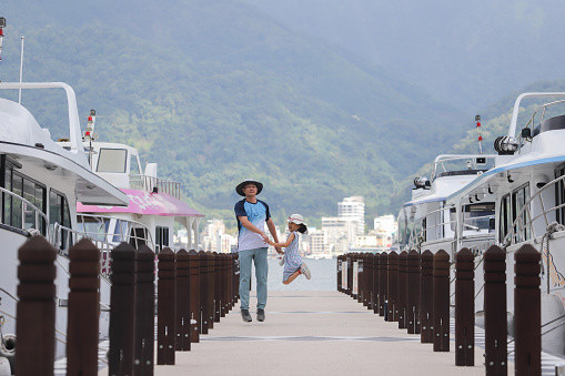 An Asian father and daughter are playing on the pier of Sun Moon Lake. The father lifts his daughter up and kisses her. Sun Moon Lake is a famous tourist attraction in Taiwan, located in Nantou County in central Taiwan.