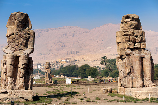 Colossi of Memnon, Luxor, River Nile, Egypt. 
Two massive stone statues of the Pharaoh stand at the front of the ruined Mortuary Temple of Amenhotep III, largest temple in the Theban Necropolis. The River Nile has always and continues to be a lifeline for Egypt. Trade, communication, agriculture, water and now tourism provide the essential ingredients of life - from the Upper Nile and its cataracts, along its fertile banks to the Lower Nile and Delta. In many ways life has not changed for centuries, with transport often relying on the camel on land and felucca on the river