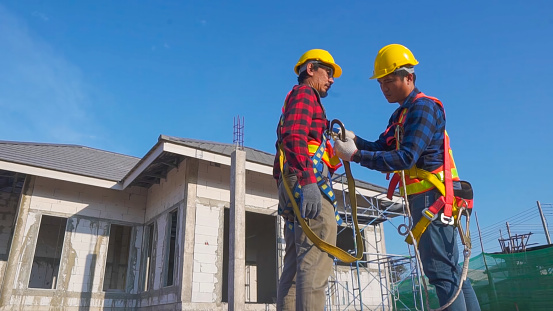 Asian two workers helping each other wearing fall protection. height teamwork concept.