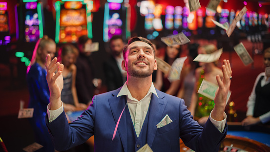 Portrait of an Excited Young Man Catching Money that is Flying From the Sky. Successful Gambler Won a Jackpot in a Casino. Concept of Gambling, Betting, Finance, Luxury and Success