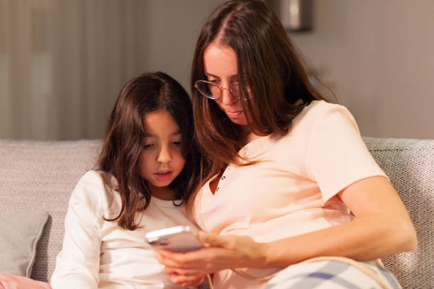 istock Mother and daughter watching the cell phone sitting on the sofa with front view 1922390001