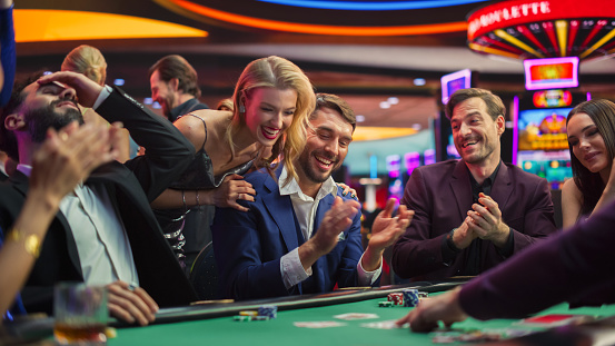 Intense Win in a Poker Game on a Casino Floor Championship. Handsome Man Has Stronger Hand and Beats Opponents with His Card Deal. Triumphant WInner Shaking Hands and Celebrating