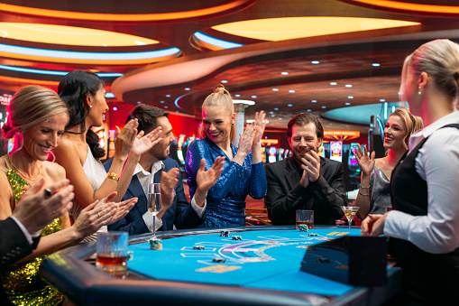 Diverse Group of Glamorous People Playing Game of Blackjack at Stylish Casino. Wealthy Patrons Having Good time Luxury Evening on Casino Floor, Betting, Sociolizing. Handsome Gentleman Wins Jackpot