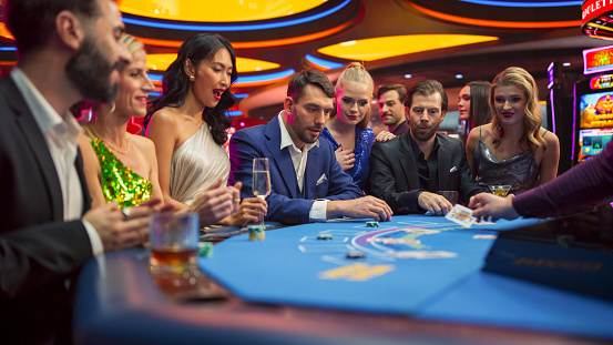 Diverse Group of Glamorous People Playing Game of Blackjack with Professional Female Croupier Dealer at Casino. Patrons Having Good Luxury Time Placing Betts. Handsome Man Wins Jackpot