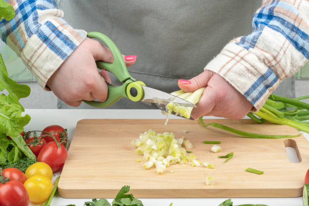 istock Female hands with kitchen scissors cut green onions. 1922410111