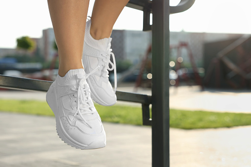Woman in stylish sneakers sitting on railing outdoors, closeup. Space for text