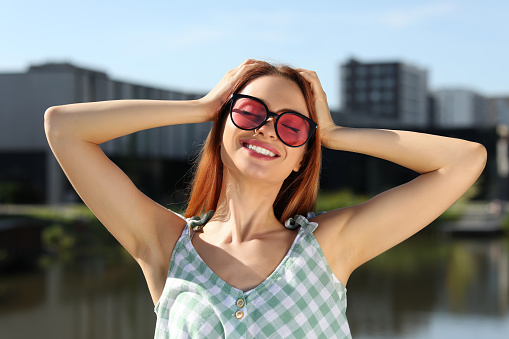 Beautiful smiling woman in sunglasses near river on sunny day