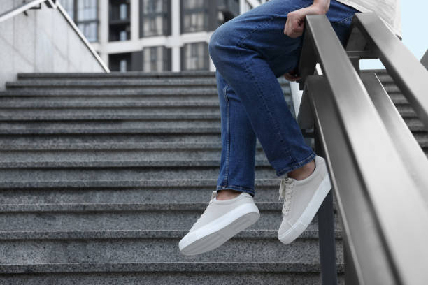 istock Man in stylish sneakers sitting on railing outdoors, closeup. Space for text 1922439525