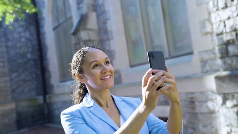 Multiracial woman by historic building with camera phone