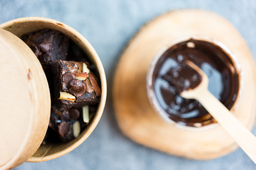 Delicious chocolate brownie topped with almond and chocolate chip in a paper brown bowl box.
