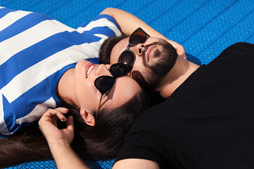 Beautiful smiling woman and handsome man in sunglasses on blue floor covering outdoors