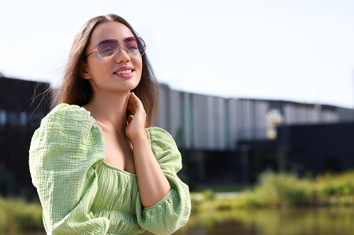 Beautiful woman in sunglasses outdoors, space for text