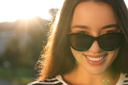 Beautiful smiling woman in sunglasses outdoors, space for text